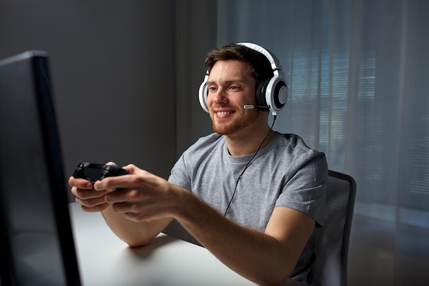 technology, gaming, entertainment, let&amp;#39;s play and people concept - happy young man in headset with controller gamepad playing computer game at home and streaming playthrough or walkthrough vid