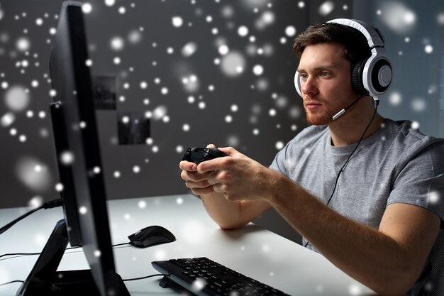 technology, gaming, entertainment, let's play and people concept - young man in headset with controller gamepad playing computer game at home and streaming playthrough or walkthrough video over snow