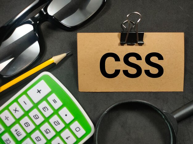 Teksti CSS Cascading Style Sheet kirjoitettu ruskealle kortille suurennuslasikynälaskimen ja lasien kanssa mustalla taustalla