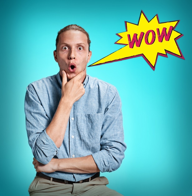 The surprised young man in blue shirt over blue studio background