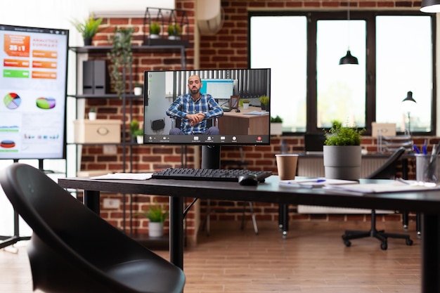 Tietokone näyttää videopuhelun miehen kanssa työpöydällä toimistossa. Online-videoneuvottelu etäkeskusteluun kollegan kanssa monitorilla yrityksen työpaikalla. Videoneuvottelukokous
