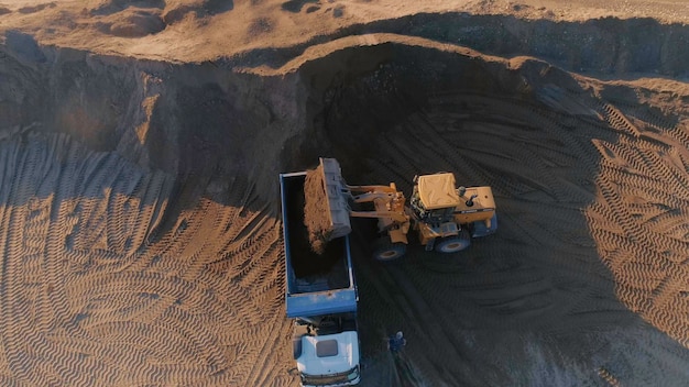 Top view of excavator with dump truck at quarry scene excavator fills dump truck at quarry with