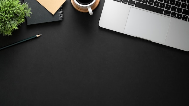 Top view of workplace with laptop, copy space, stationery and coffee cup on black table