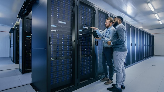Two men in a data center with one of them pointing at a tablet.