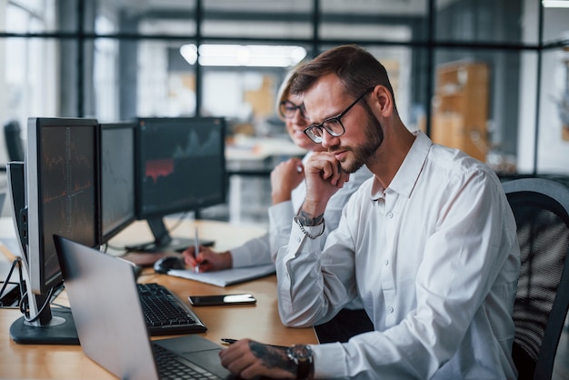 Two stockbrokers in formal clothes works in the office with financial market.
