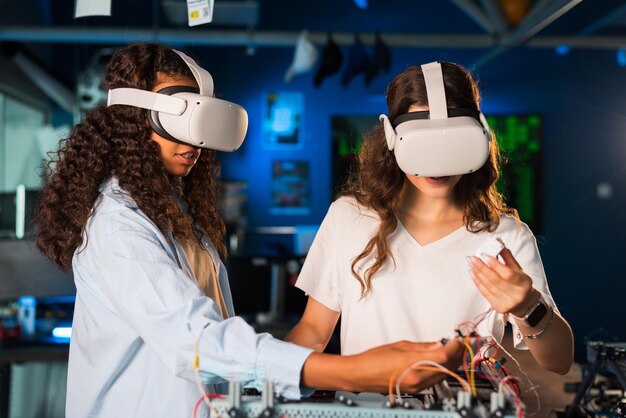 Two young women in VR glasses doing experiments in robotics in a laboratory Robot on the table