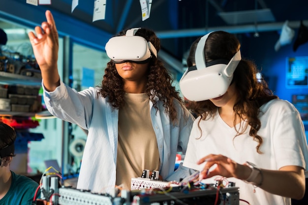 Two young women in VR glasses doing experiments in robotics in a laboratory Robot on the table