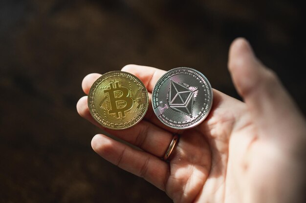 Unrecognizable hand holding an ethereum and a bitcoin cryptocoins in 3d rendering on dark background with copy space.