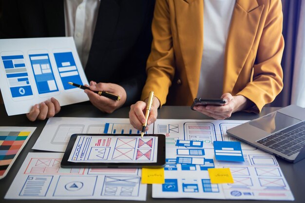 UX-kehittäjä ja UI-suunnittelija ideoivat mobiilisovelluksen käyttöliittymän wireframe-suunnittelua asiakkaan ohjeistuksen ja värikoodin kanssa toimistossaxA
