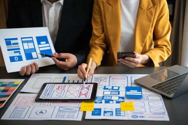 UX-kehittäjä ja UI-suunnittelija ideoivat mobiilisovelluksen käyttöliittymän wireframe-suunnittelua asiakkaan ohjeistuksen ja värikoodin kanssa toimistossaxA