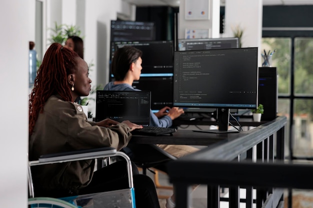 Wheelchair user typing script code on computer, working with cloud computing terminal window. Disabled web developer writing artificial intelligence algorithm in it big data company office.