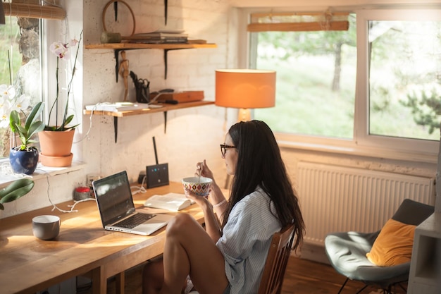 Woman eating food while using laptop on table at home