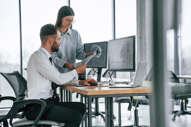 Woman is standing and holding documents Two employees are working in the office together
