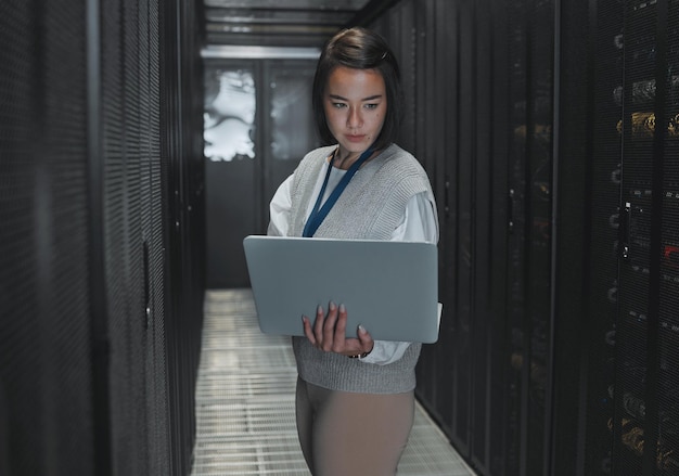 Woman with laptop server room and IT engineer and datacenter with software update and programming Tech industry cybersecurity and network with Asian female setting up firewall and database
