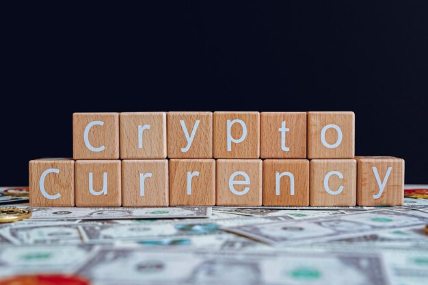 Wooden blocks with the text Cryptocurrency on a black background and crypto banknotes scattered on