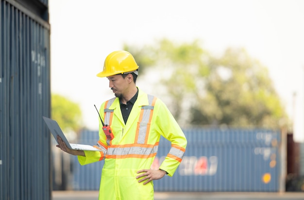 Workers in the import and export industry holding a laptop and standing on the front of container