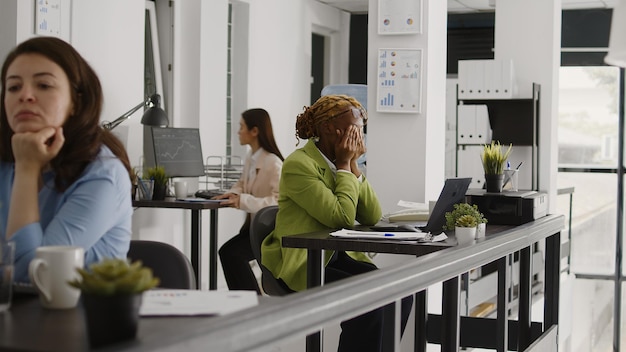 Worried entrepreneur working with headache at desk, feeling sick and frustrated in startup office. Young manager dealing with painful migraine and being under pressure, business agency.