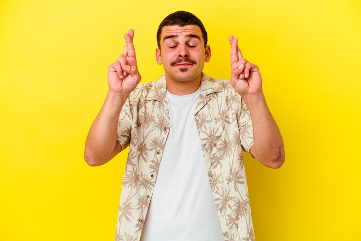 Kuva young cool man isolated on yellow wall crossing fingers for having luck