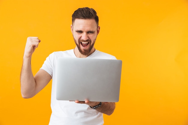 young excited man posing isolated over yellow wall using laptop computer