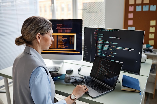 Young female progammer checking code on laptop screen