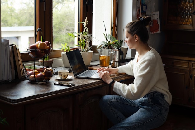 Young freelancer working on laptop at home woman using computer on the kitchen for work distant