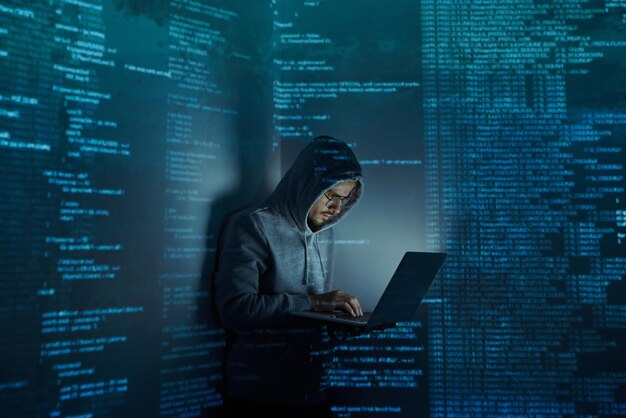 Young man in hooded shirt using computer while standing against dark background