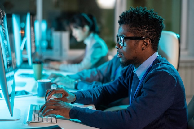 Young serious businessman in eyeglasses and formalwear looking at screen of computer