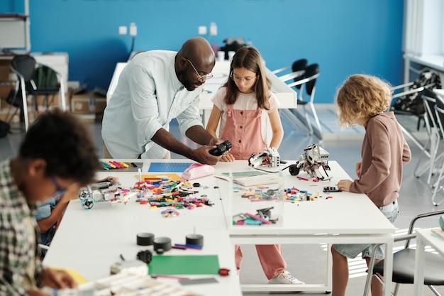 Young teacher bending over table with constructor details and schoolgirl