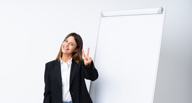 young woman giving a presentation on white board smiling and showing victory sign