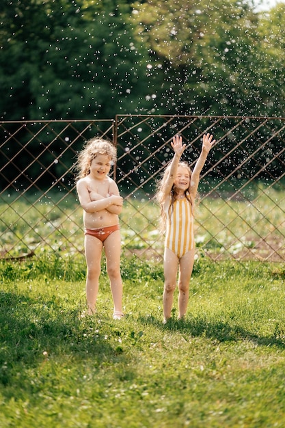 01032022 Bar Ukraine two little sisters dressed in swimsuits are splashing with water on a sunny summer day in the yard of the house on a green background