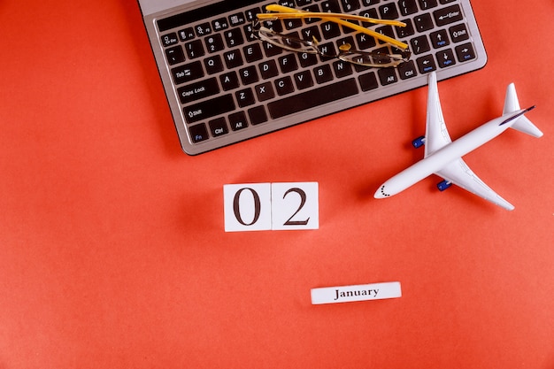 02 January calendar with accessories on business workspace office desk on computer keyboard, airplane, glasses red background