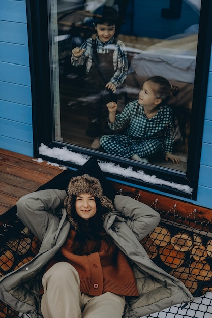 020124 Bar Ukraine young woman dressed in warm country clothes on the background of a country house for vacation with two chilren enjoying the winter view of the village