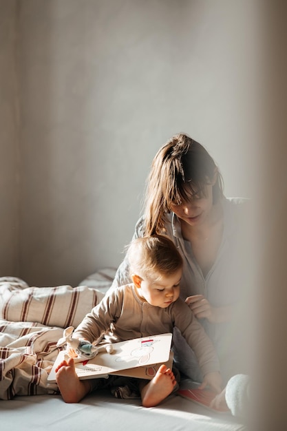 02032022 Vinnitsa Ukraine young mother and little daughter woke up in bed having fun hugging looking at a book