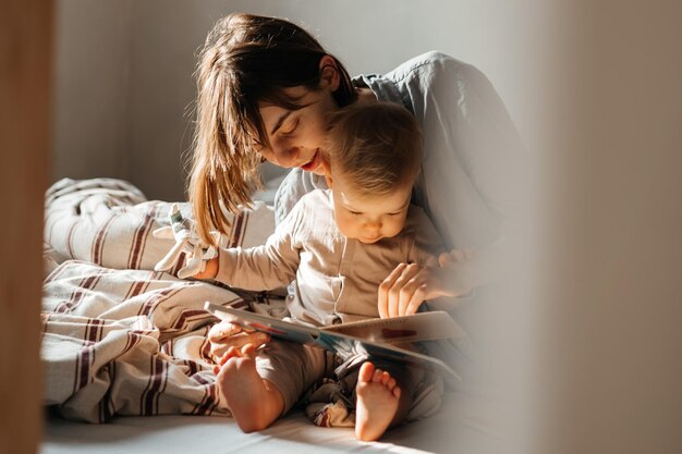 02032022 Vinnitsa 우크라이나 젊은 엄마와 어린 딸이 책을 보고 껴안고 즐겁게 침대에서 일어났습니다.