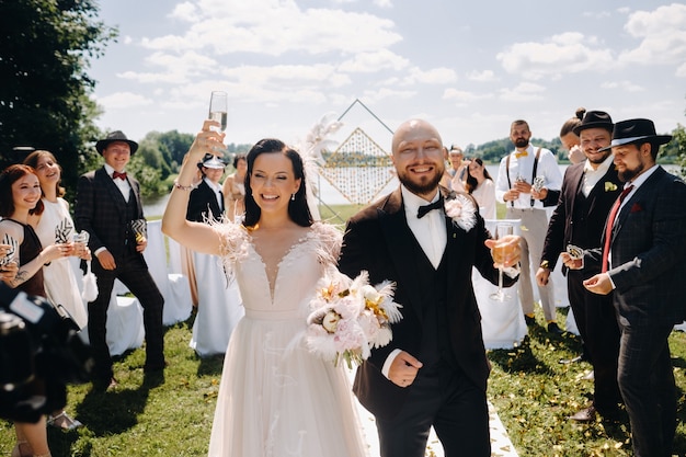 08.07.2021。 Nesvizh.Belarus。結婚式の後、グラスワインを片手に幸せな結婚式のカップルがゲストを通ります。