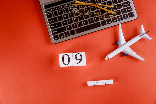 09 januari kalender met accessoires op zakelijke werkruimte bureau op computertoetsenbord, vliegtuig, glazen rode achtergrond