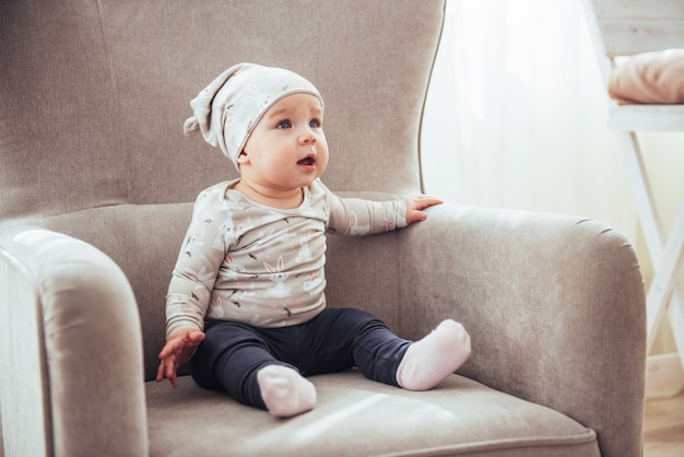 1 jaar meisje, gekleed in stijlvolle kleding, zittend in een vintage stoel in de kamer.