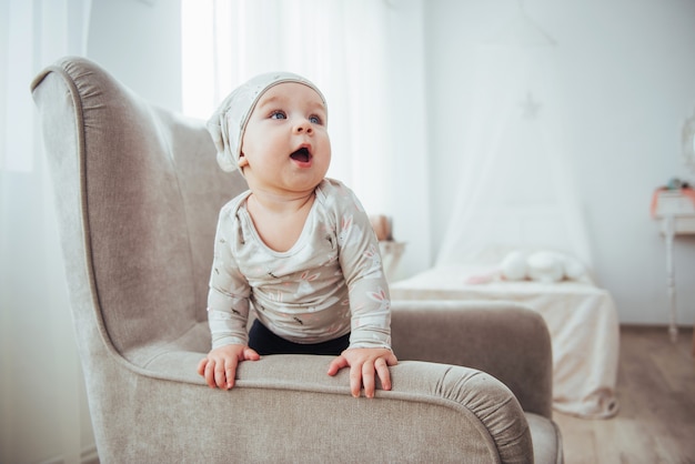 1 jaar meisje, gekleed in stijlvolle kleding, zittend in een vintage stoel in de kamer.