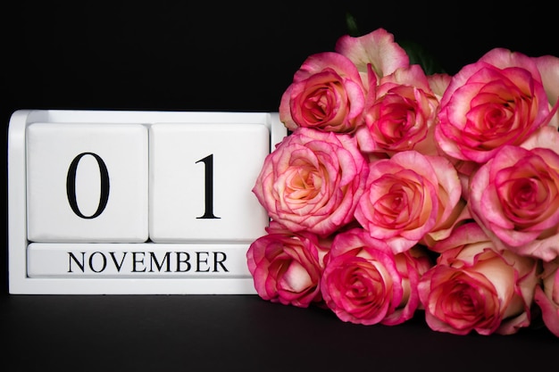 1 november houten kalender, wit op een zwarte achtergrond, roze rozen liggen in de buurt.