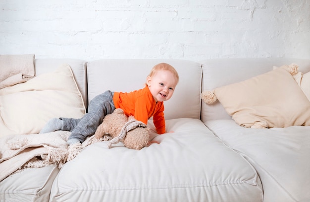 Photo 1 white little girl in an orange blouse on a light sofa, emotions of a child