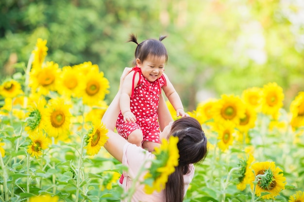 1 살짜리 아기와 그녀의 어머니는 태양 꽃 정원에서 함께 행복을 느낀다.