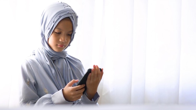 10 jaar oud Aziatisch moslimkind staat naast het raam. Mooi moslimmeisje in hijab en traditie