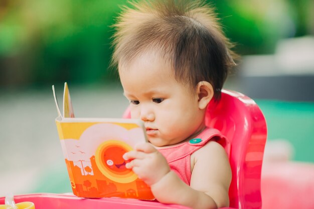 10 maanden babymeisje die een boek in de tuin lezen