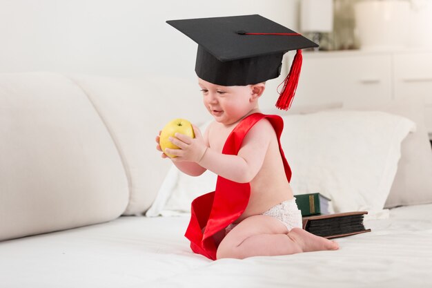 10 months old baby boy in graduation cap and ribbon holding yellow apple