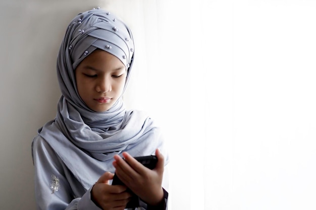 Photo 10 years old asian muslim kid stand beside the window.beautiful muslim girl in hijab and traditional