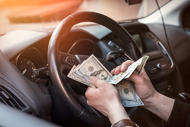 100 dollar bills in male hand, man inside in the car. Concept of bribes, insurance or rent, buy