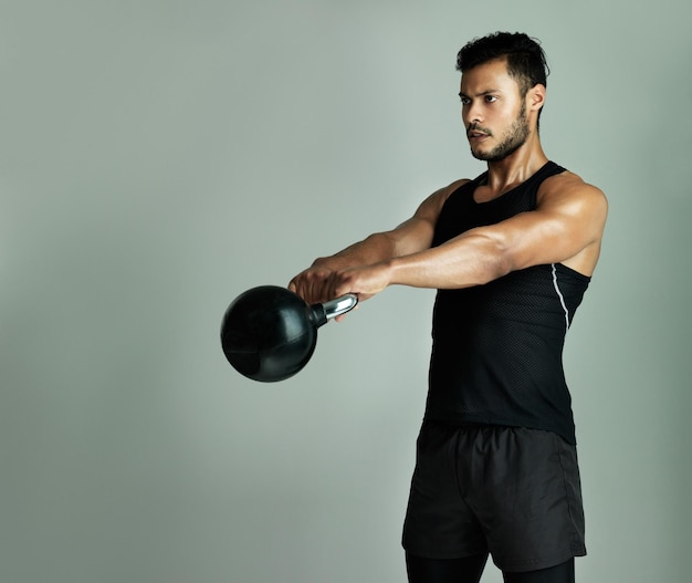 100 focused on his training Studio shot of a young man working out with a kettle bell against a gray background