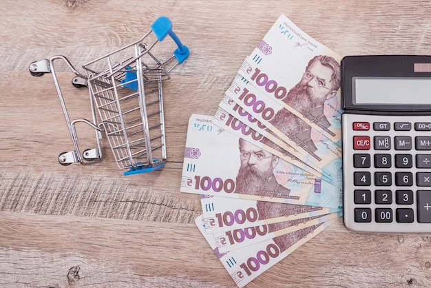 1000 hryvnia with a calculator and a shopping cart on a wooden background. Shopping concept.