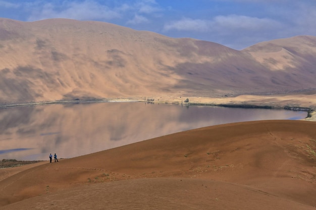 Photo 1153 sumu barun jaran lake in badain jaran desert-dark water reflecting cloudy sky and dunes china