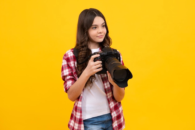 12 13 14세 십대 소녀가 노란색 배경 위에 디지털 카메라나 DSLR을 들고 있습니다.